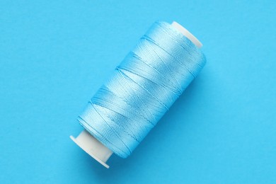 Photo of Spool of sewing thread on light blue background, top view