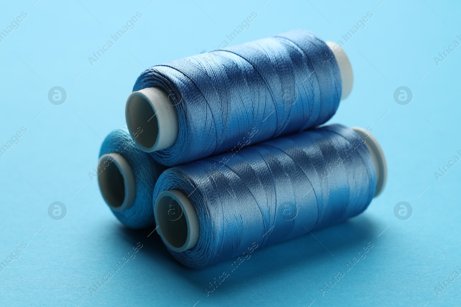 Photo of Spools of sewing threads on light blue background, closeup