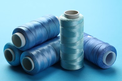 Photo of Spools of sewing threads on light blue background, closeup