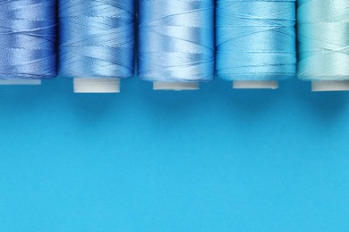 Photo of Spools of sewing threads on light blue background, flat lay. Space for text