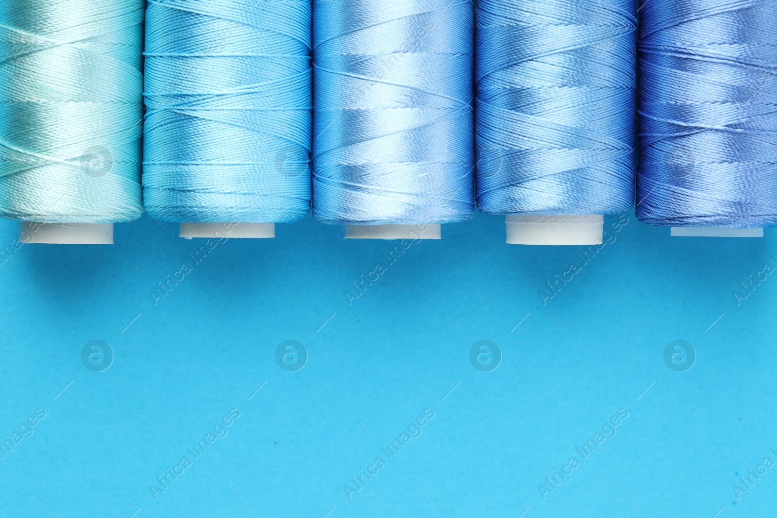 Photo of Spools of sewing threads on light blue background, flat lay. Space for text