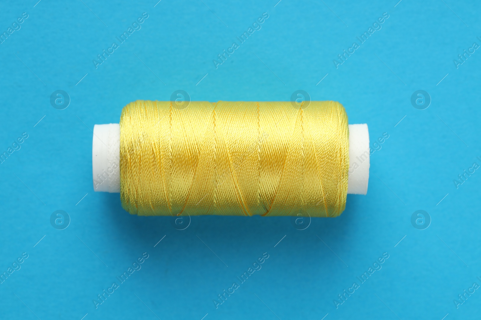 Photo of Spool of yellow sewing thread on light blue background, top view