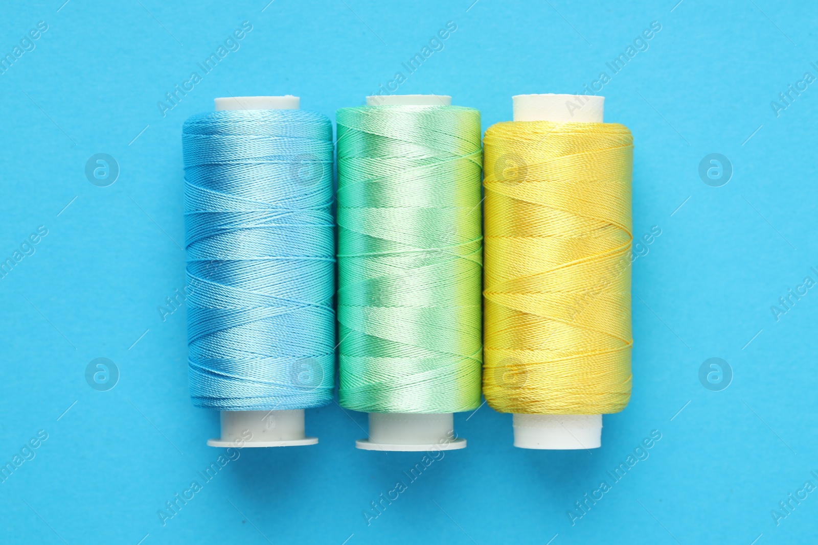 Photo of Different spools of sewing threads on light blue background, flat lay