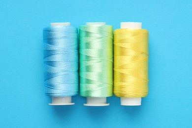 Photo of Different spools of sewing threads on light blue background, flat lay