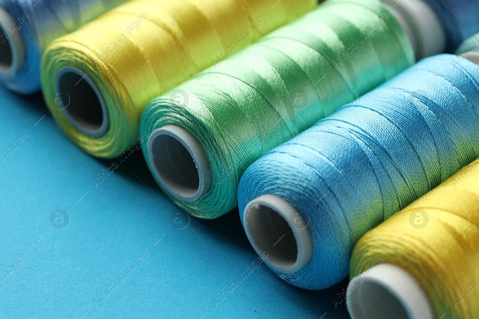 Photo of Different spools of sewing threads on light blue background, closeup