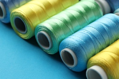 Photo of Different spools of sewing threads on light blue background, closeup