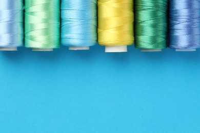 Photo of Different spools of sewing threads on light blue background, flat lay. Space for text