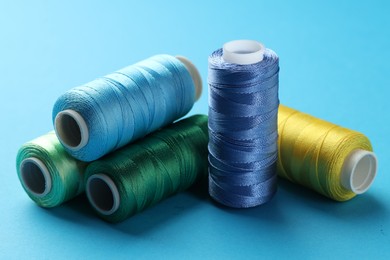 Photo of Different spools of sewing threads on light blue background, closeup