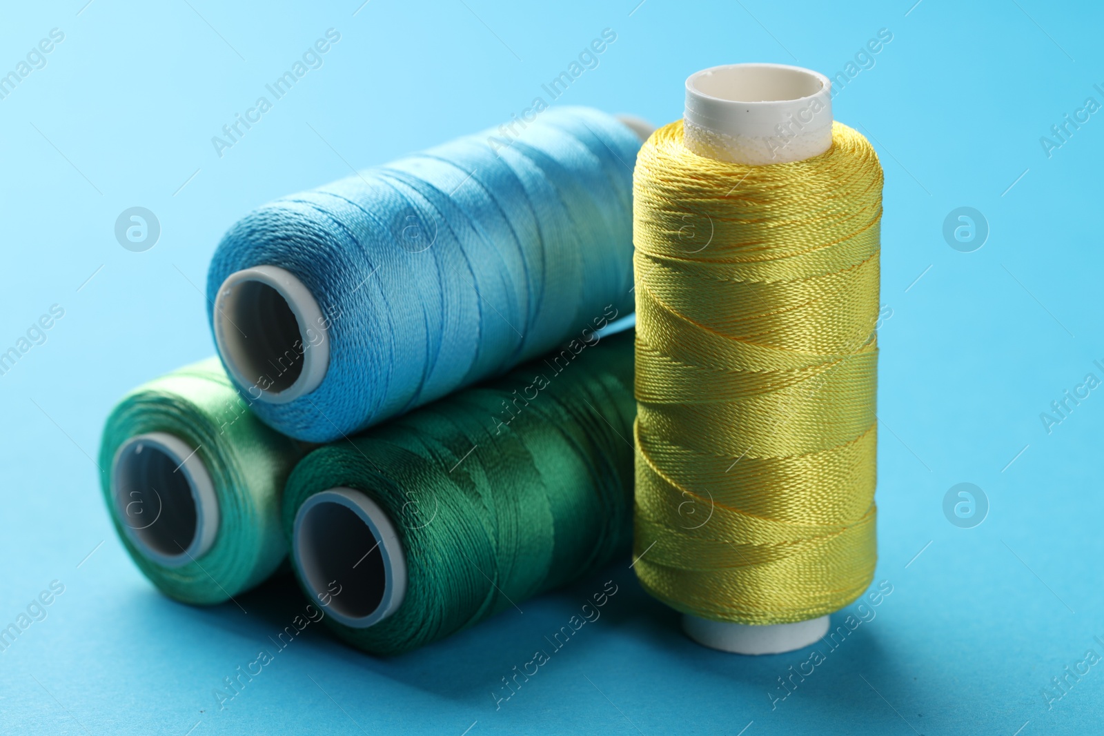 Photo of Different spools of sewing threads on light blue background, closeup