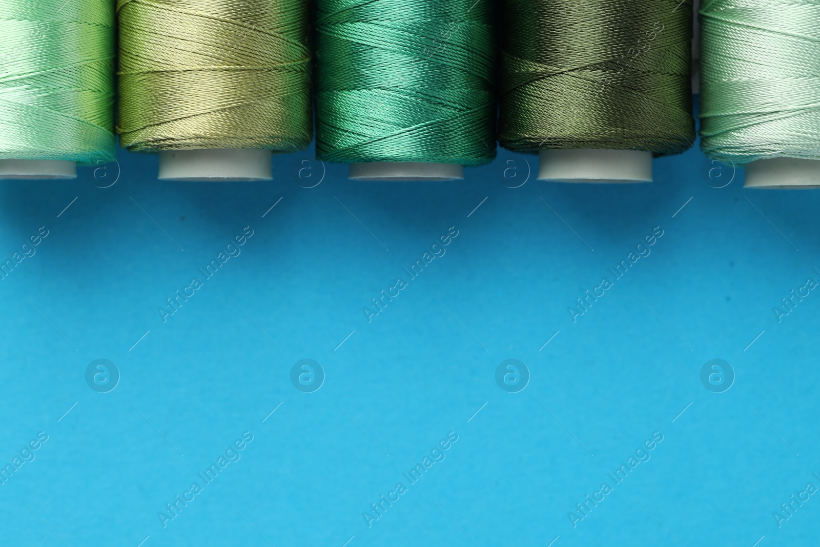 Photo of Different spools of sewing threads on light blue background, flat lay. Space for text