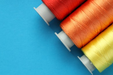 Photo of Different spools of sewing threads on light blue background, flat lay. Space for text