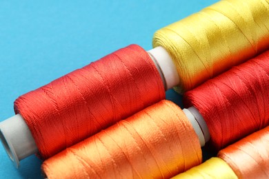 Photo of Different spools of sewing threads on light blue background, closeup