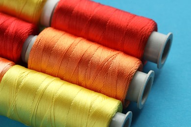 Photo of Different spools of sewing threads on light blue background, closeup