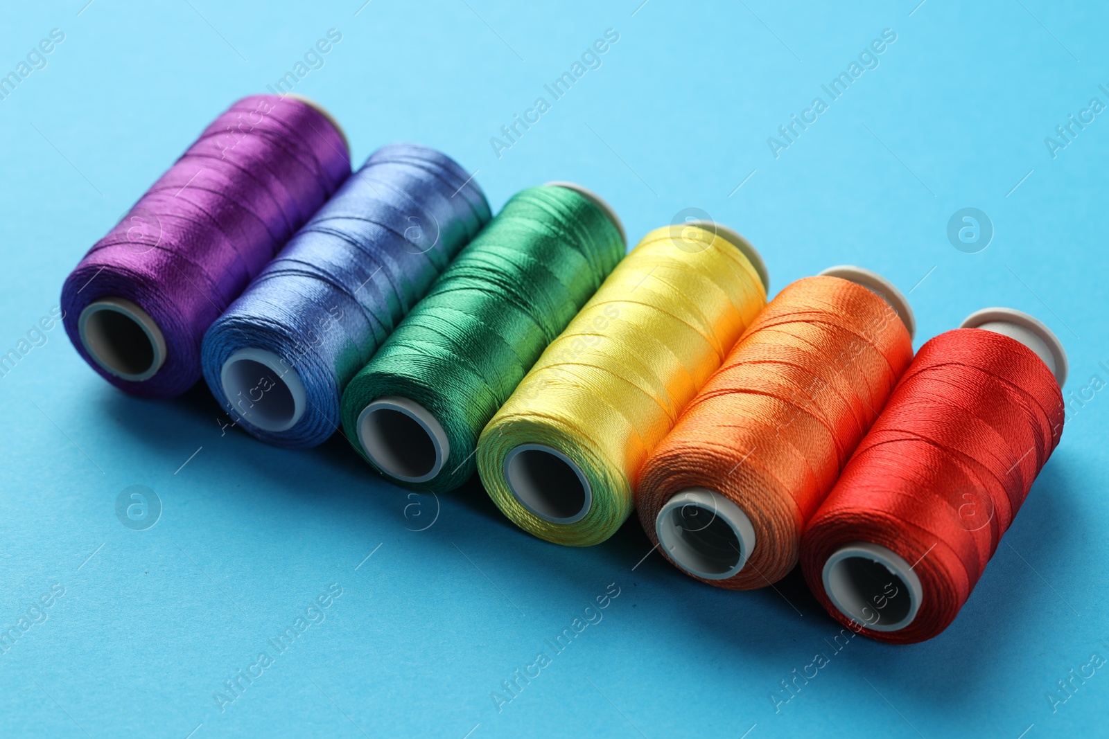 Photo of Different spools of sewing threads on light blue background, closeup