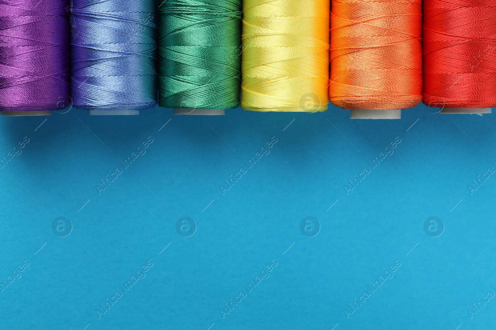 Photo of Different spools of sewing threads on light blue background, flat lay. Space for text