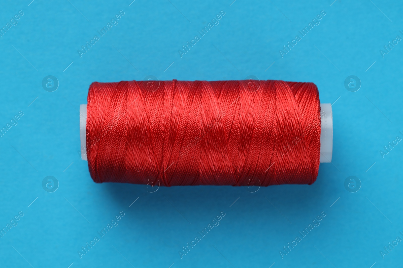 Photo of Spool of red sewing thread on light blue background, top view