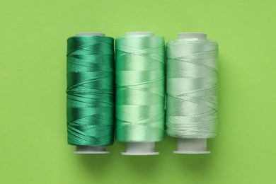 Photo of Spools of sewing threads on light green background, flat lay