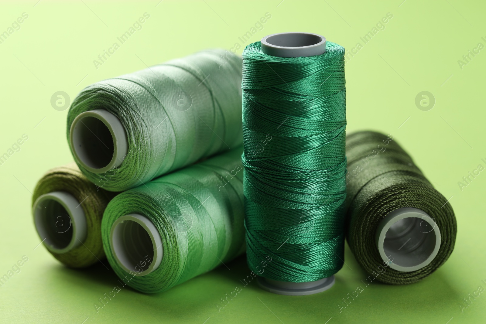 Photo of Spools of sewing threads on light green background, closeup