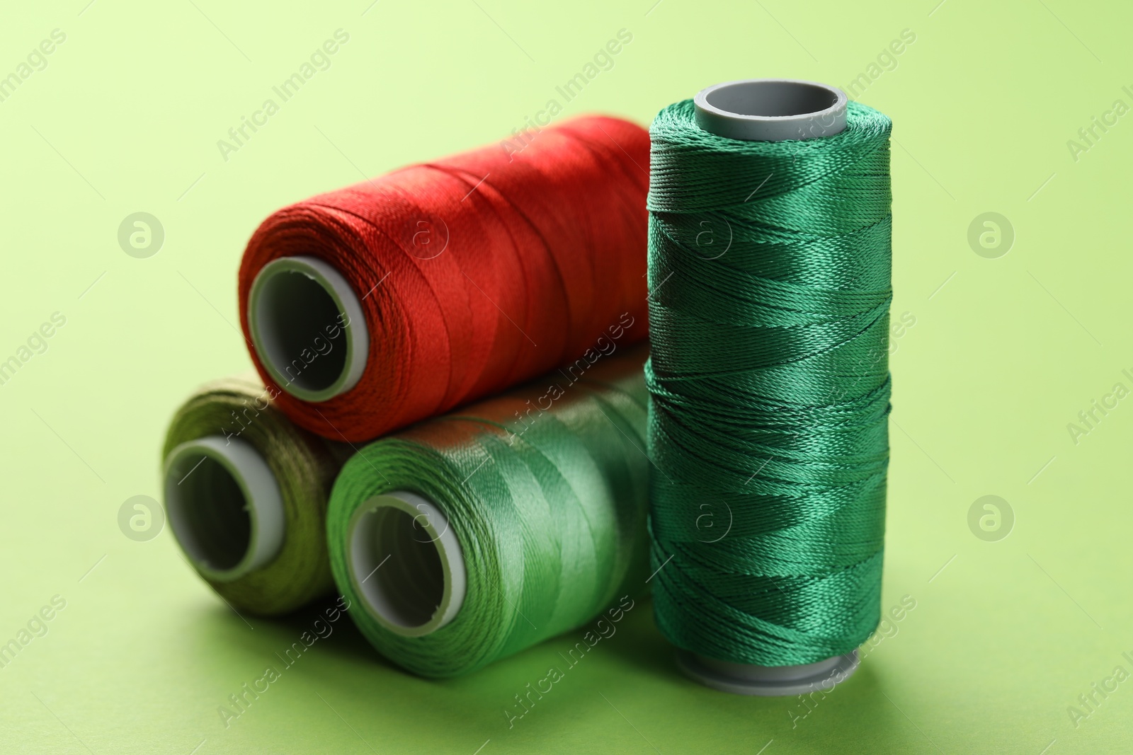 Photo of Spools of sewing threads on light green background, closeup