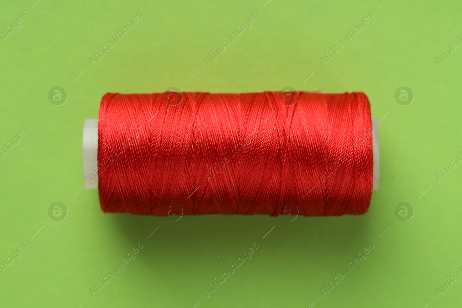 Photo of Spool of red sewing thread on light green background, top view