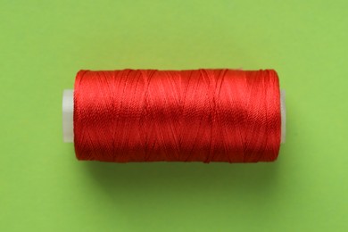 Photo of Spool of red sewing thread on light green background, top view