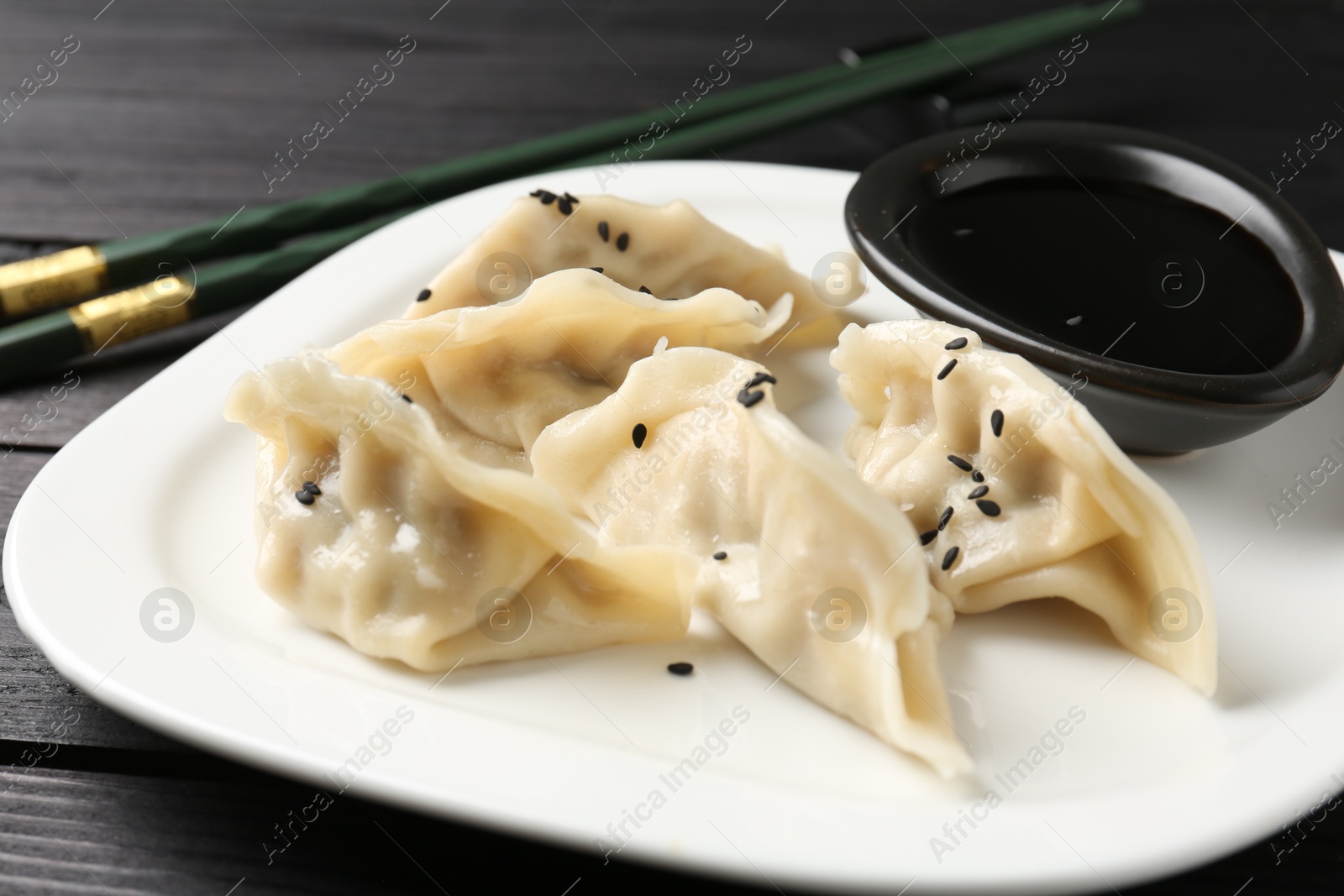 Photo of Delicious gyoza dumplings with sesame seeds served on black wooden table, closeup