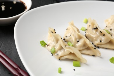 Photo of Delicious gyoza dumplings with chives and sesame seeds served on black table, closeup