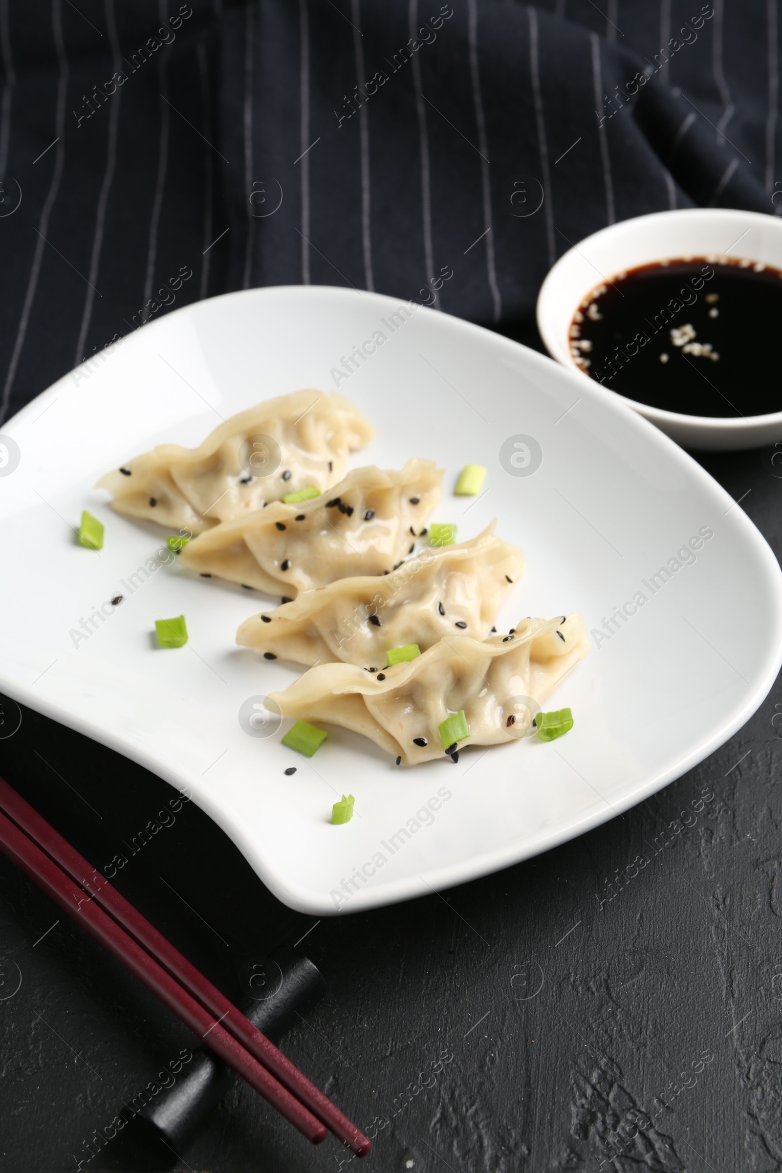 Photo of Delicious gyoza dumplings with chives and sesame seeds served on black table, closeup