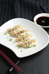 Photo of Delicious gyoza dumplings with chives and sesame seeds served on black table, closeup