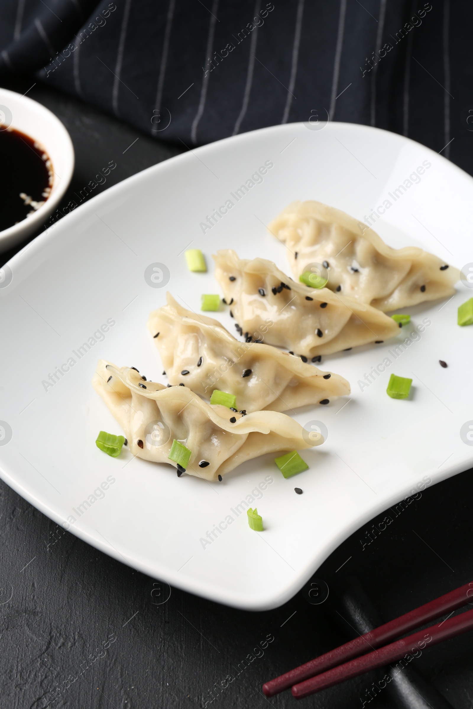 Photo of Delicious gyoza dumplings with chives and sesame seeds served on black table, closeup