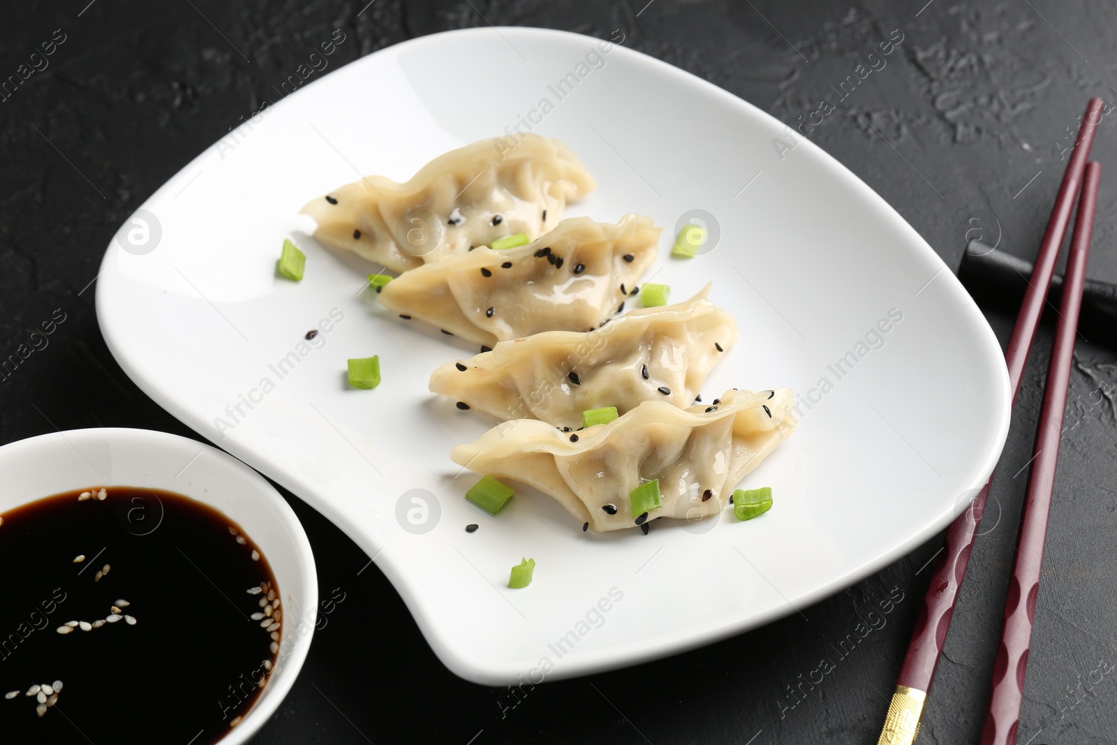 Photo of Delicious gyoza dumplings with chives and sesame seeds served on black table, closeup