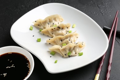 Photo of Delicious gyoza dumplings with chives and sesame seeds served on black table, closeup