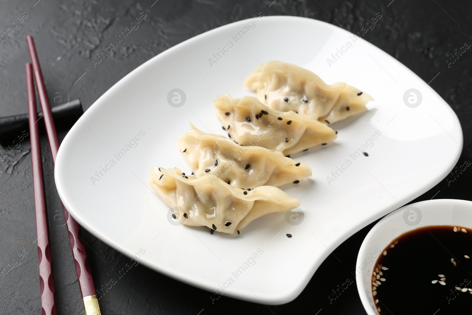 Photo of Delicious gyoza dumplings with sesame seeds served on black table, closeup