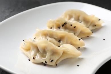 Photo of Delicious gyoza dumplings with sesame seeds served on black table, closeup