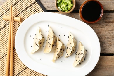 Photo of Delicious gyoza dumplings with sesame seeds served on wooden table, top view