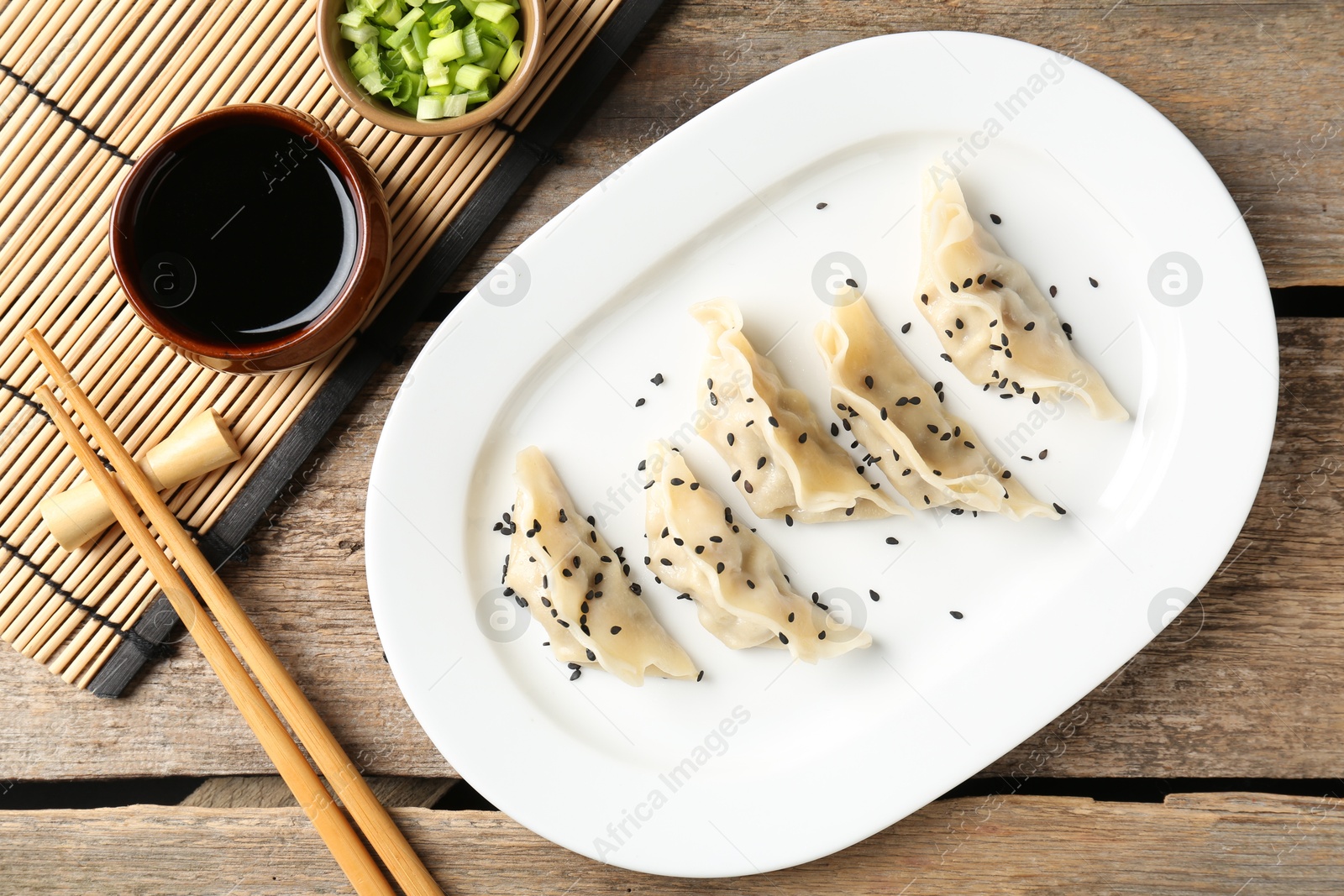 Photo of Delicious gyoza dumplings with sesame seeds served on wooden table, top view