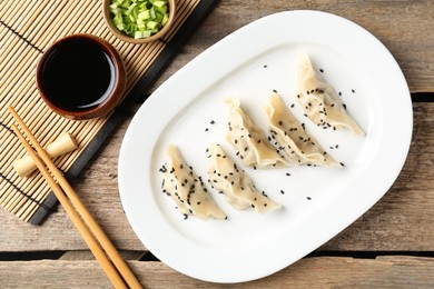 Photo of Delicious gyoza dumplings with sesame seeds served on wooden table, top view