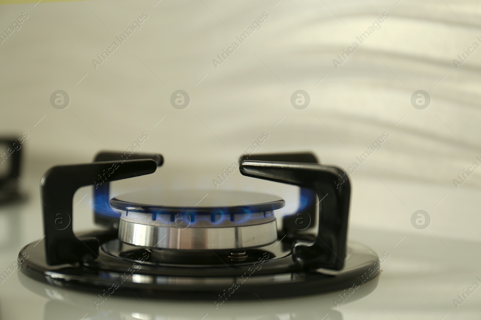 Photo of Gas burner of modern stove with burning blue flame, closeup