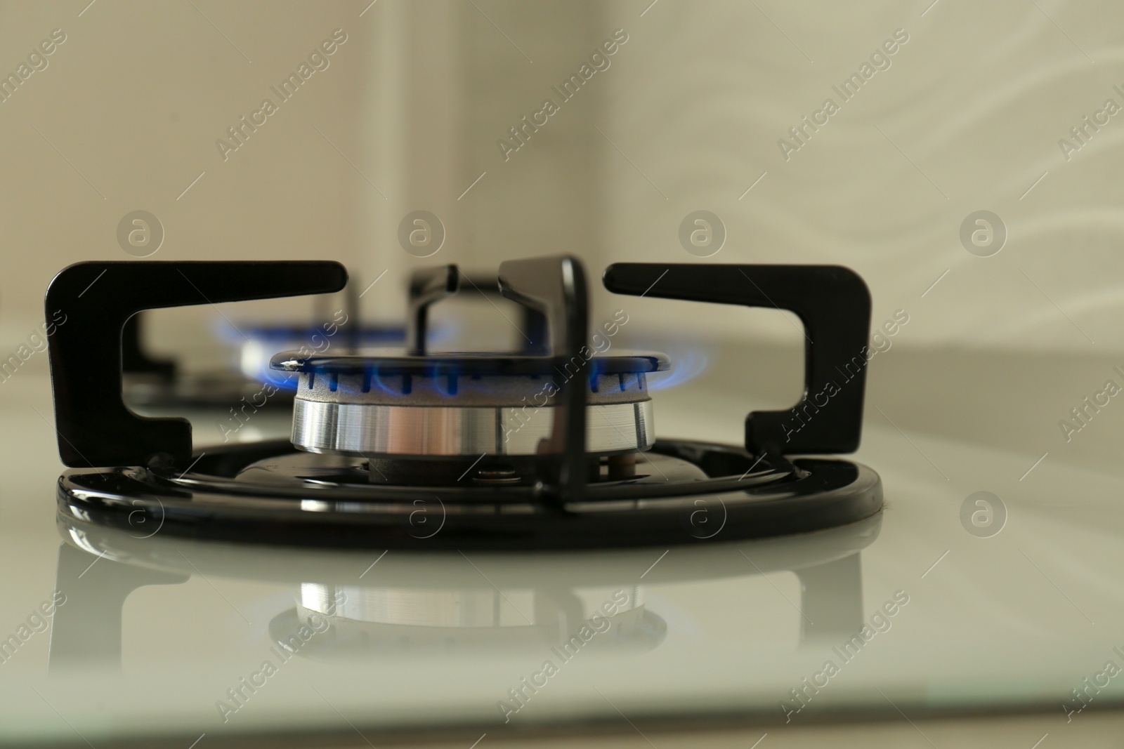 Photo of Gas burner of modern stove with burning blue flame, closeup