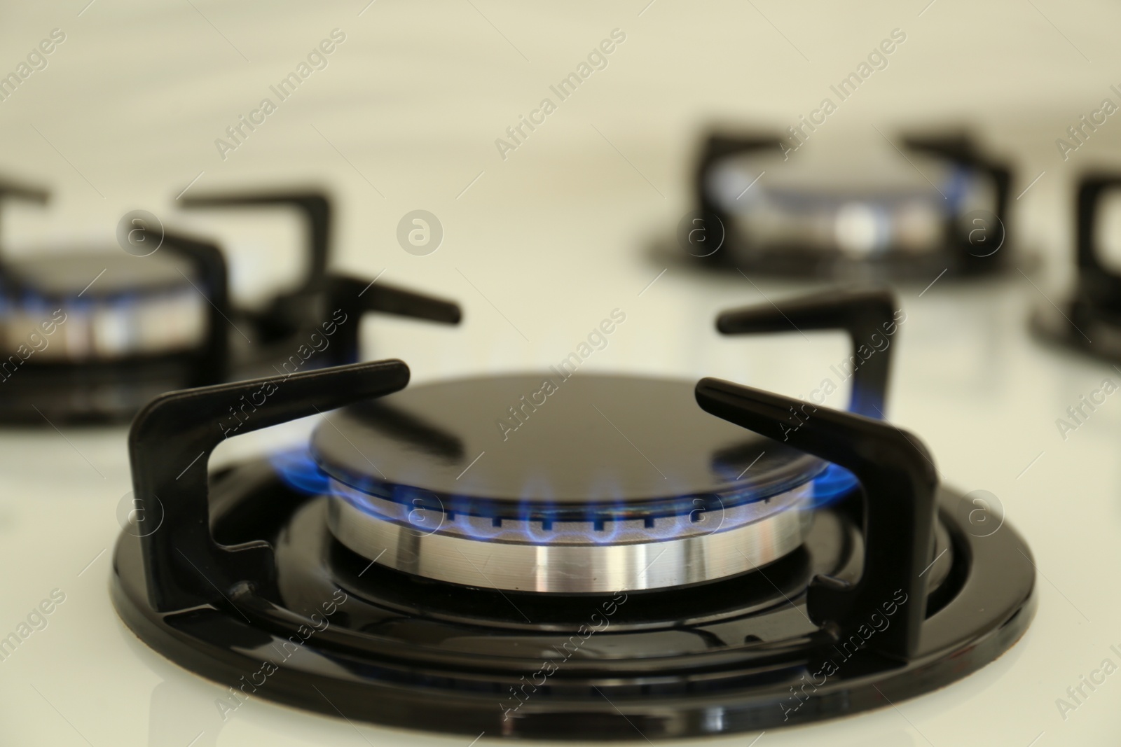 Photo of Gas burner of modern stove with burning blue flame, closeup