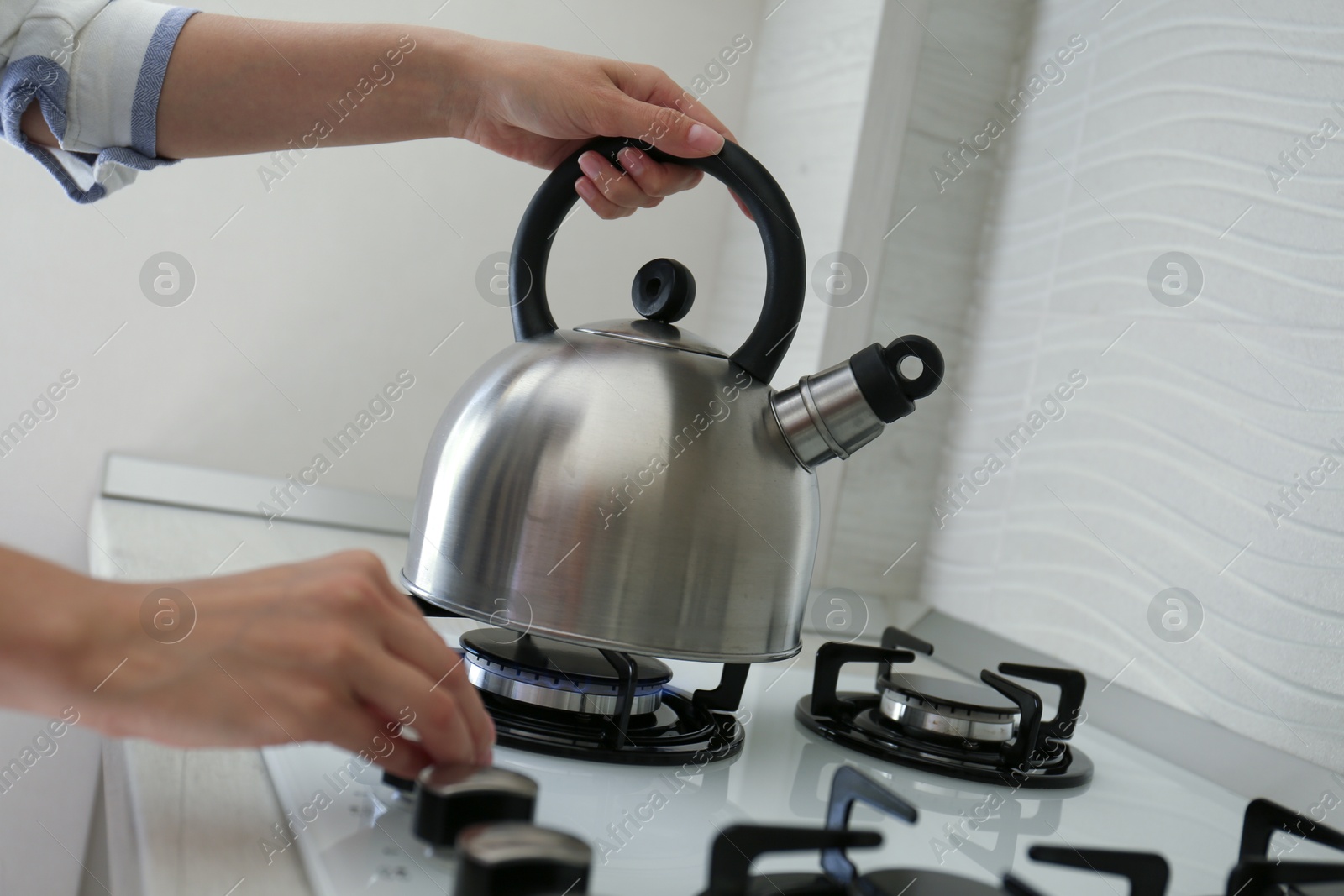 Photo of Woman putting kettle on gas stove in kitchen, closeup