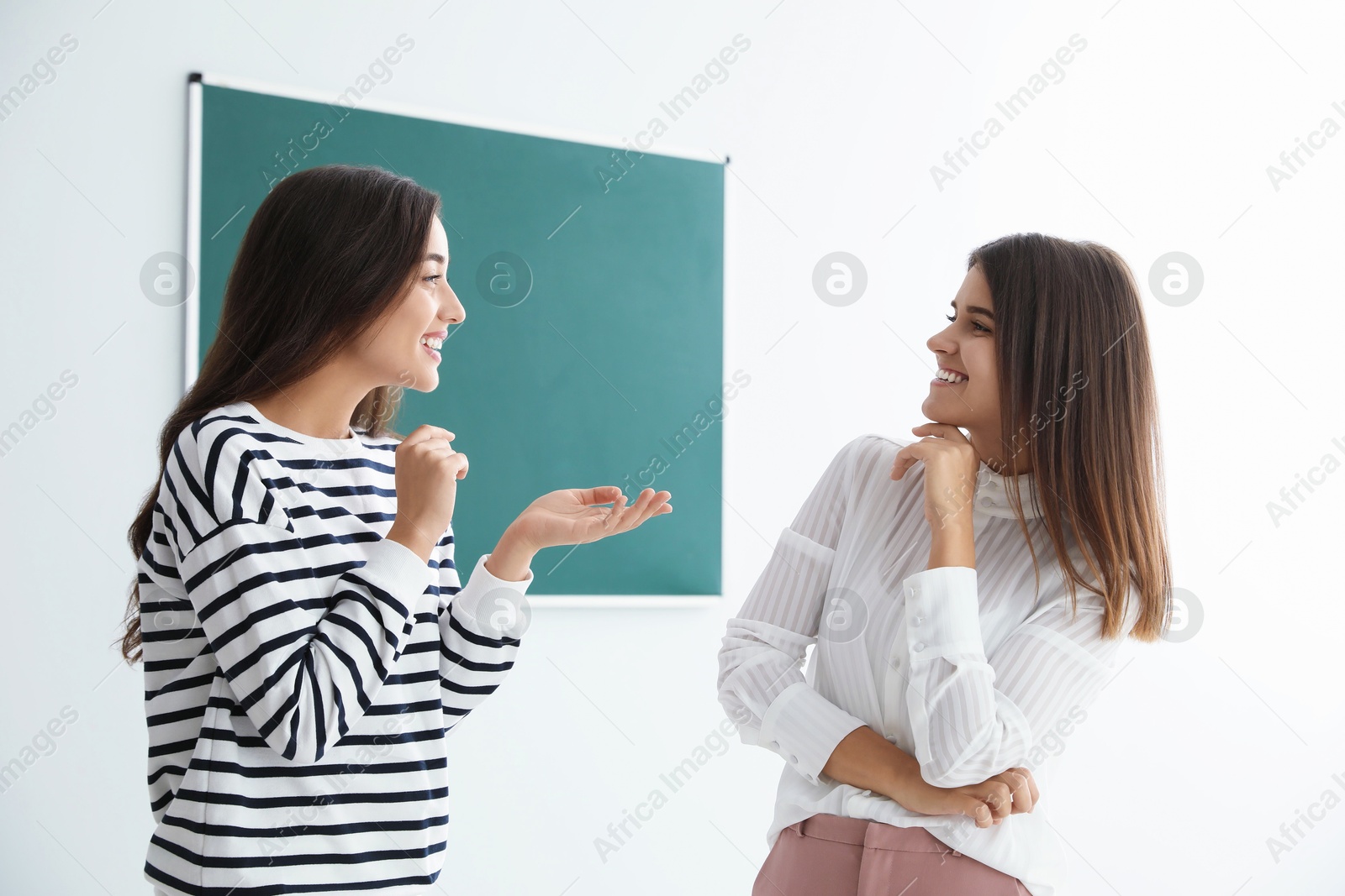 Photo of Young women talking near green chalkboard in classroom