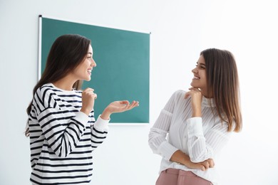 Young women talking near green chalkboard in classroom