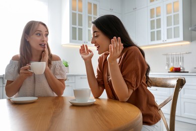 Young women talking while drinking tea at table in kitchen