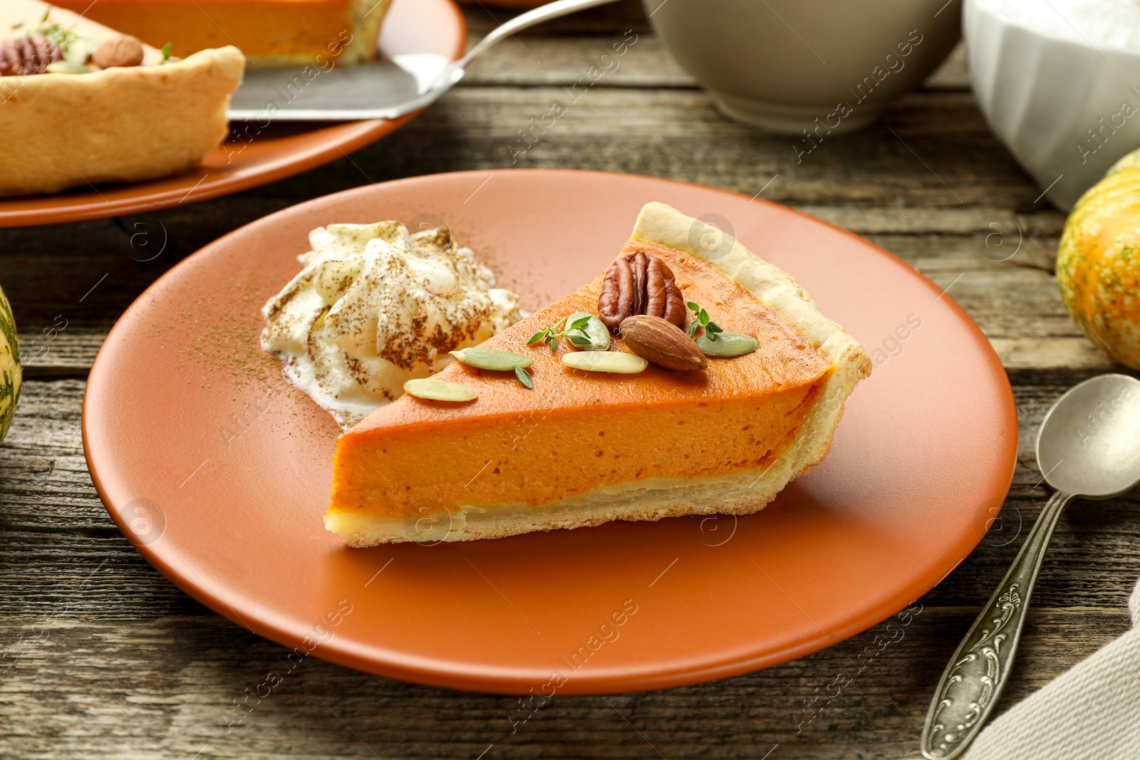 Photo of Piece of tasty homemade pumpkin pie with whipped cream, seeds and nuts on wooden table, closeup