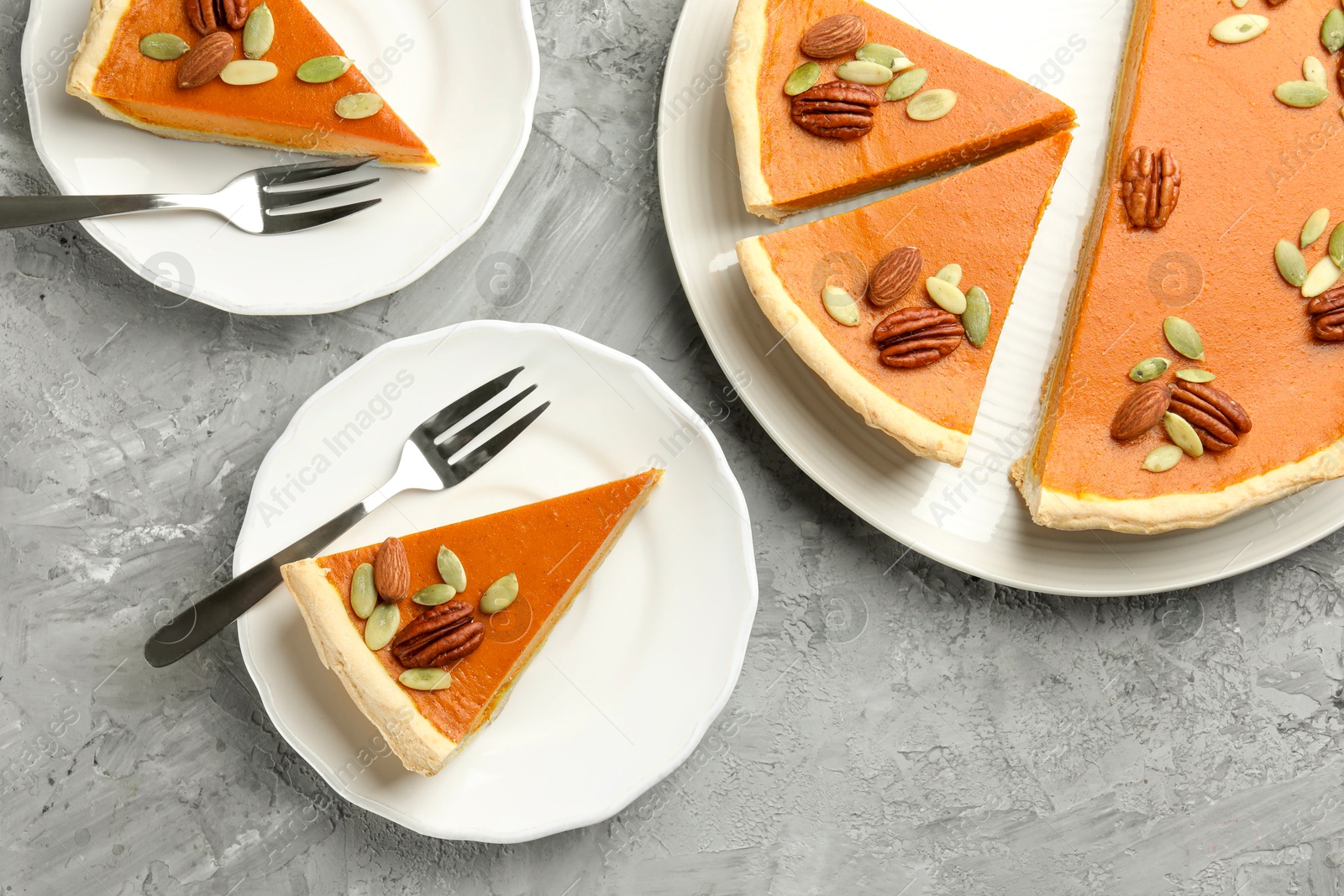 Photo of Pieces of tasty homemade pumpkin pie with seeds and nuts on grey table, top view