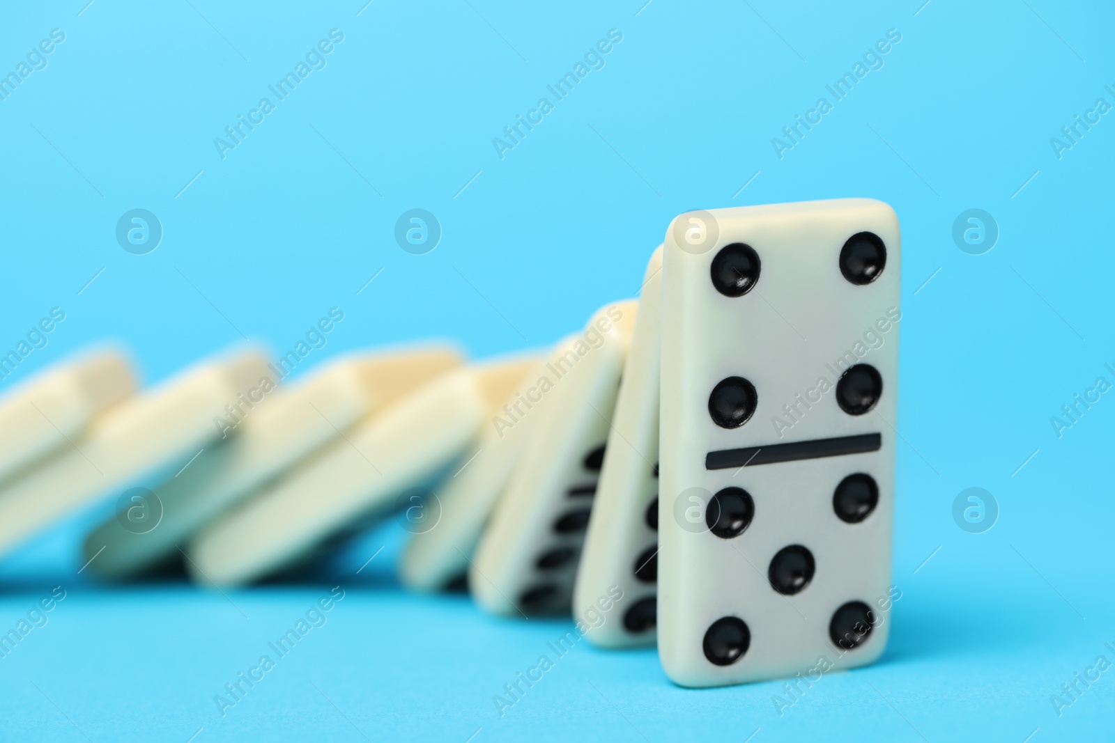 Photo of Dominoes falling on light blue background, closeup