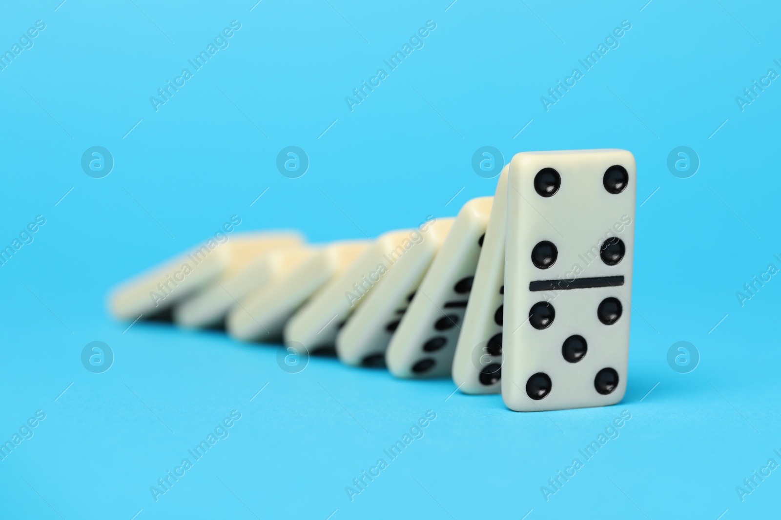 Photo of Domino effect. Tiles falling on light blue background