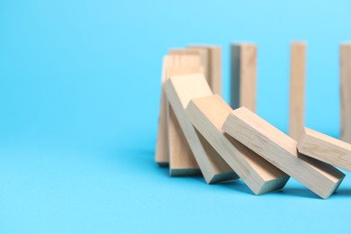 Photo of Domino effect. Wooden blocks falling on light blue background, closeup. Space for text