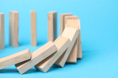 Photo of Domino effect. Wooden blocks falling on light blue background, closeup. Space for text